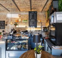 Kaffeehaus mit Backsteinwänden, Theke mit Speisen- und Getränkeangebot, Pflanzen in gastronomischen Räumen.