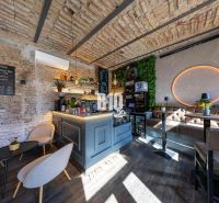 Innenraum eines Gastronomiebereichs mit Bartresen, Ziegelwänden und einem Boden in Holzoptik.