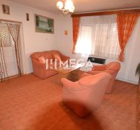 Wohnzimmer in einem Einfamilienhaus mit orangefarbenen Möbeln und Teppich, Vorhänge an den Fenstern.
