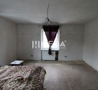 Schlafzimmer in einem Einfamilienhaus mit abblätterndem Boden und lila Vorhängen.