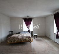 Ein Zimmer mit einem Bett, einem Stuhl und einem Tisch, einem Boden mit Holzdekor, Vorhänge an den Fenstern.