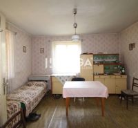 Ein Zimmer in einem Einfamilienhaus mit Tapeten, einem Tisch, einem Bett, einer Vitrine und einem Boden mit Holzdekor.