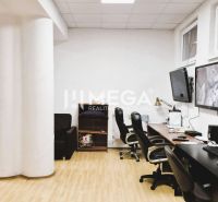 Ein Büro mit einem Boden in Holzoptik, Tischen, Stühlen und Bildschirmen an der Wand.