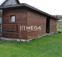 Holzbau neben einem Einfamilienhaus in der Stadt Krásny Brod auf grünem Gras.