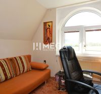 Ein Arbeitszimmer in einem Einfamilienhaus mit einem orangefarbenen Sofa, einem Sessel und einem Blick aus dem Fenster.