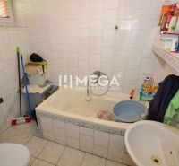 Ein Badezimmer im Einfamilienhaus mit einer Badewanne, einem Waschbecken und Kosmetikartikeln auf dem Regal.