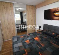 Schlafzimmer mit Bett und Schrank mit Schiebetüren, Boden mit Holzdekor.