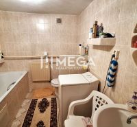 Badezimmer mit weißer Badewanne und Waschmaschine in einem Einfamilienhaus, gefliest mit hellem Fliesenbelag.
