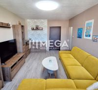 Wohnzimmer in einer 3-Zimmer-Wohnung mit Holzboden, gelbem Sofa und Regalen.