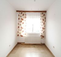 Ein Zimmer in einem Einfamilienhaus mit Fenster, Blumen-Vorhängen und Fliesen.