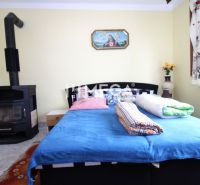 Interieur eines Einfamilienhauses mit Bett, Kachelofen und bunten Accessoires.