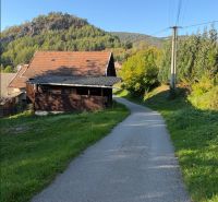 Die Straße in Košecké Podhradie führt an Häusern vorbei, gesäumt von Grün und Hügeln. Grundstücke - Wohnen.