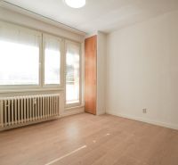 Ein Zimmer in einer Einzimmerwohnung mit einem Holzboden, weißen Wänden und Fenstern.