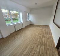 Ein Zimmer mit großen Fenstern und einem Holzboden in einer Zweizimmerwohnung.