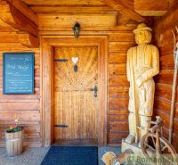Ein Holzhaus in Machulince, mit Skulpturen und einer Wandtafel am Eingang.