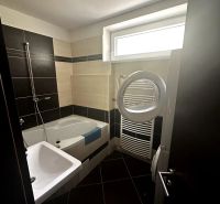 Badezimmer in einer 2-Zimmer-Wohnung mit Badewanne, Waschbecken und Waschmaschine; schwarze und beige Fliesen.