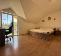Ein Schlafzimmer im Dachgeschoss eines Einfamilienhauses mit einem Bett, einem Boden in Holzoptik und einem Schreibtisch.
