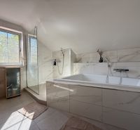 Ein Badezimmer in einem Einfamilienhaus mit einer Badewanne und einer Dusche, umgeben von Fliesen.