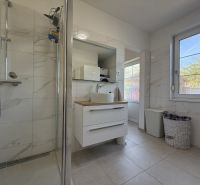 Ein Badezimmer in einem Einfamilienhaus mit weißen Fliesen, einer Dusche und Stauraum.