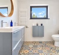 Badezimmer mit Mosaikboden, modernem Waschbecken und Fenster in einer Einzimmerwohnung.