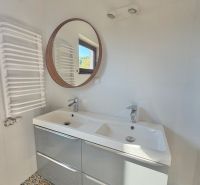Das Badezimmer in der Einzimmerwohnung enthält ein Doppelwaschbecken, einen runden Spiegel und gemusterte Fliesen.