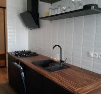 Küche in einer 2-Zimmer-Wohnung mit schwarzer Dunstabzugshaube, weißen Fliesen und einem Boden in Holzoptik.