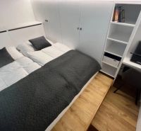Schlafzimmer in einer Einzimmerwohnung mit Doppelbett und Stauraum, Boden mit Holzdekor.