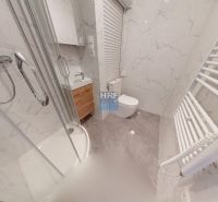 Badezimmer in einem Studio-Apartment mit Badewanne, Waschbecken, WC und Wänden mit Marmordekor.