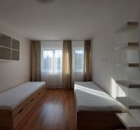 Ein Zimmer mit zwei Betten, Regalen und einem Boden in Holzoptik in einer 3-Zimmer-Wohnung.