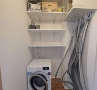 Technikraum in einer 3-Zimmer-Wohnung mit Waschmaschine und Regalen, Boden mit Holzdekor.