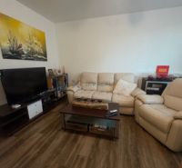 Wohnzimmer einer Zweizimmerwohnung mit Holzboden und bequemen Sitzgelegenheiten.