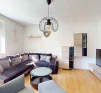 Wohnzimmer in einer 2-Zimmer-Wohnung mit Holzboden und einer Couchgarnitur.