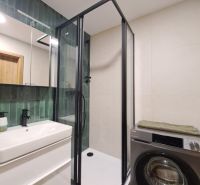 Badezimmer einer 2-Zimmer-Wohnung mit moderner Duschkabine, Waschmaschine und grünen Fliesen.