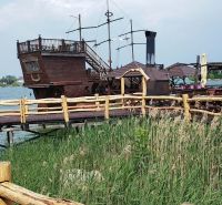 Ein Holzboot als Attraktion bei der Hütte an den Seen von Senec, hinter einem Holzzaun.