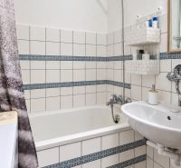 Badezimmer mit Badewanne, Waschbecken, weißen Fliesen und gemusterten Details in einer 3-Zimmer-Wohnung.
