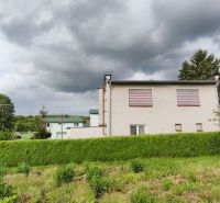 Ein Einfamilienhaus in Nenince, umgeben von dichtem Grün und Bäumen unter einem bewölkten Himmel.