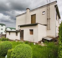 Ein Einfamilienhaus in Nenince mit Rasen und Sträuchern unter einem bewölkten Himmel.
