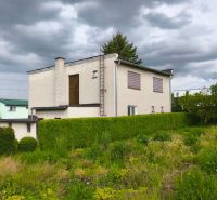 Ein Einfamilienhaus in Nenince, umgeben von Grün und einer Hecke unter einem bewölkten Himmel.