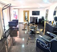 Friseursalon mit schwarzem Granitboden, großen Spiegeln und bequemen Stühlen.