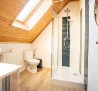 Ein Badezimmer im Dachgeschoss mit Waschbecken, Dusche und einem Boden in Holzoptik.