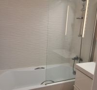Badezimmer in einer 3-Zimmer-Wohnung mit Badewanne, weißen Fliesen und einem Boden in Holzoptik.