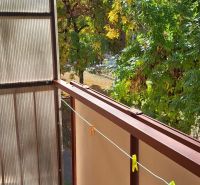 Balkon einer 3-Zimmer-Wohnung in Komárno mit Blick auf grüne Bäume.
