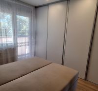 Schlafzimmer in einer 3-Zimmer-Wohnung mit einem großen Kleiderschrank und einem Fenster mit Vorhängen.
