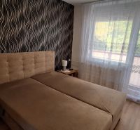 Schlafzimmer mit gepolstertem Bett, gemusterte Tapete, Vorhänge, Boden mit Holzdekor.