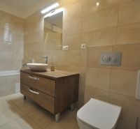 Badezimmer mit Badewanne, Waschbecken auf Holzdekor und beigen Fliesen in einer 3-Zimmer-Wohnung.