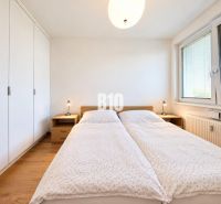 Helles Schlafzimmer mit großem Bett, Kleiderschrank und Boden mit Holzdekor in einer Zweizimmerwohnung.