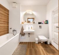 Badezimmer in einer 2-Zimmer-Wohnung mit Badewanne, Waschbecken und Boden mit Holzdekor.