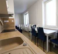 Küche in einer 2-Zimmer-Wohnung mit weißen Möbeln, blauen Stühlen und einem Boden in Holzoptik.