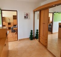 Ein Flur in einer 3-Zimmer-Wohnung mit Holzschränken und Dekorationen auf beigen Fliesen.
