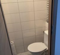 Toilette mit einfacher Verkleidung und Fliesen in einer 2-Zimmer-Wohnung.